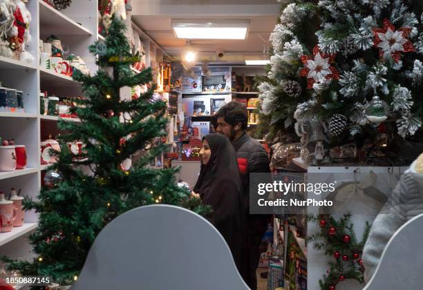 Veiled Iranian woman and her husband are looking at a Christmas tree while standing in a shop during Christmas shopping in downtown Tehran, Iran, on...