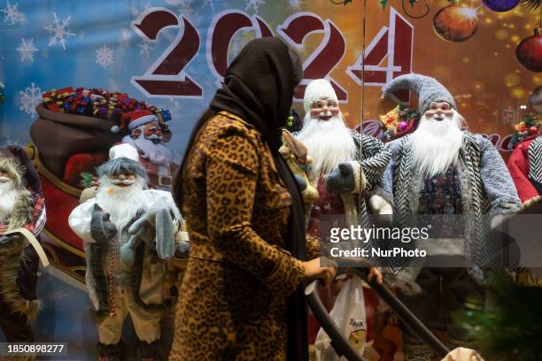 An Iranian-Christian woman is looking at a shop window decorated with statues of Santa Claus for Christmas shopping in downtown Tehran, Iran, on...