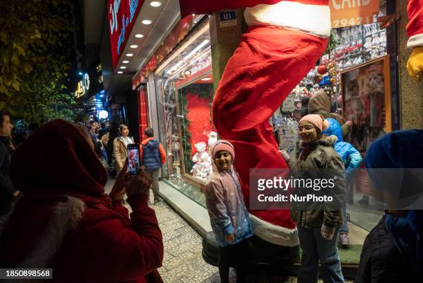 Two young Iranian girls are posing for a photograph in front of a shop decorated for Christmas shopping in downtown Tehran, Iran, on December 15,...
