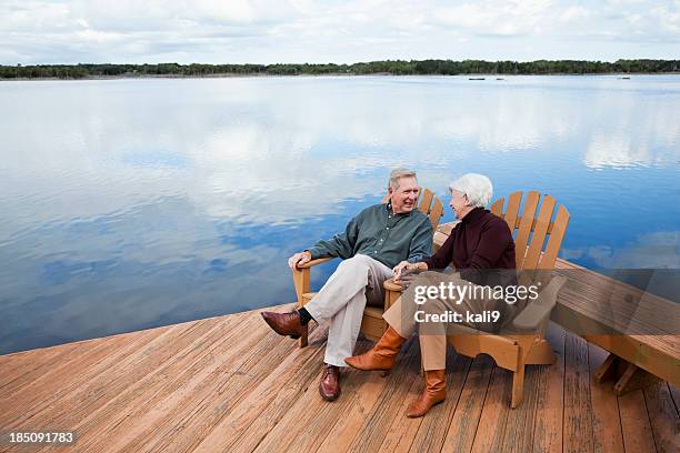 senior couple sitting by water - adirondack chair stockfoto's en -beelden