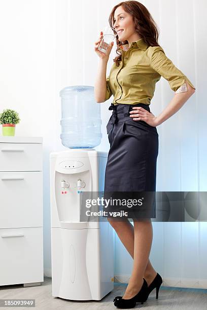 businesswoman having drink from water cooler - water cooler stockfoto's en -beelden