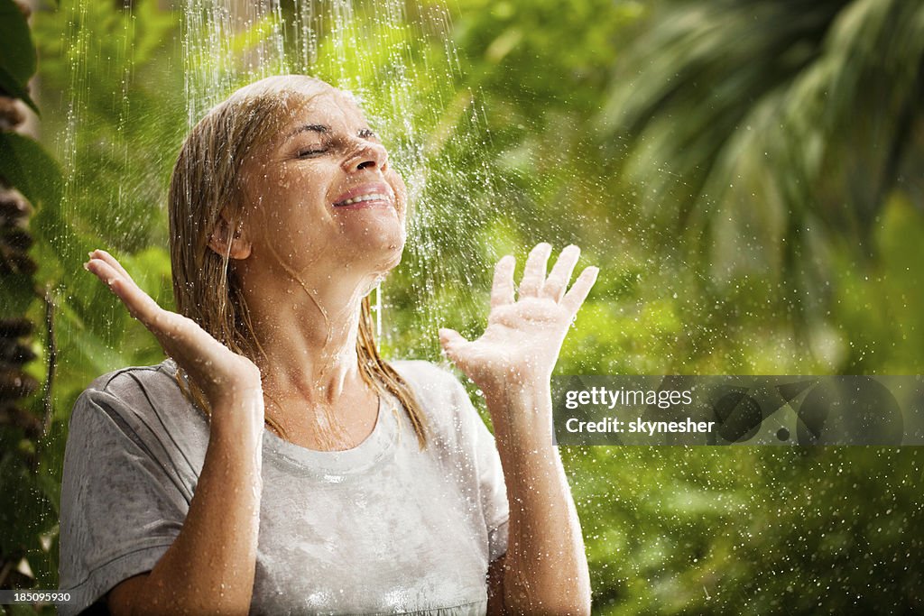 Alegre mujer tener una ducha en la naturaleza tropical.