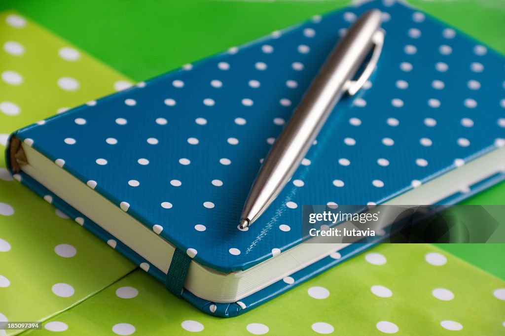 Blue spotted notebook and pen on green background