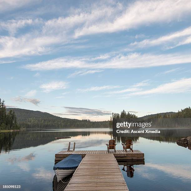 tranquil scene with lake pier and covered boat - adirondack chair stockfoto's en -beelden