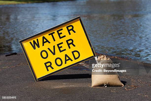 yellow “water over road” hazard sign and flooded street - flood stockfoto's en -beelden