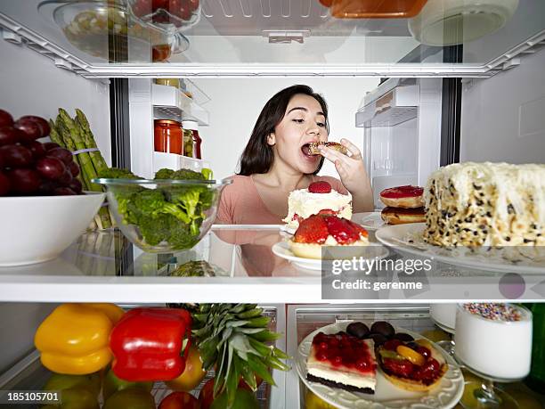 young woman eating donut - full fridge stockfoto's en -beelden