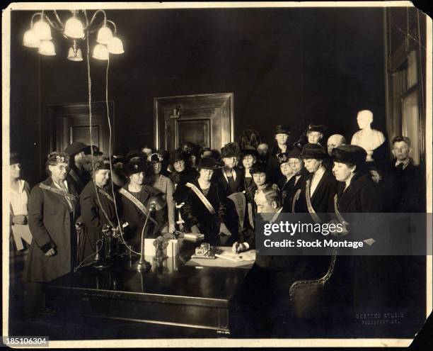 Surrounded by mostly women, many with 'Votes for Women' sashes, American politician Governor of Kentucky Edwin P. Morrow signs his states...