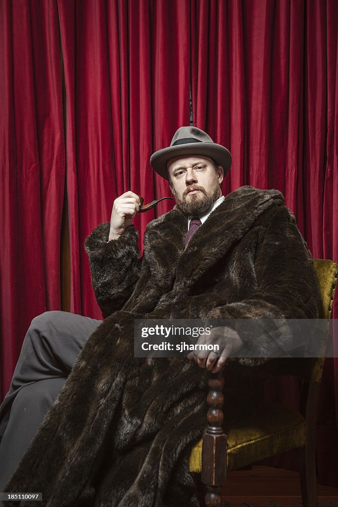 Seated Bearded Man Wearing Fedora, Fur Coat, Holding Pipe