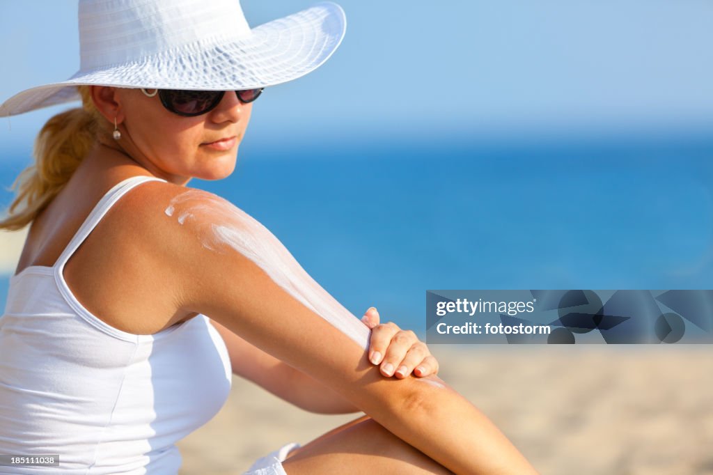 Frau benutzt Sonnencreme am Strand