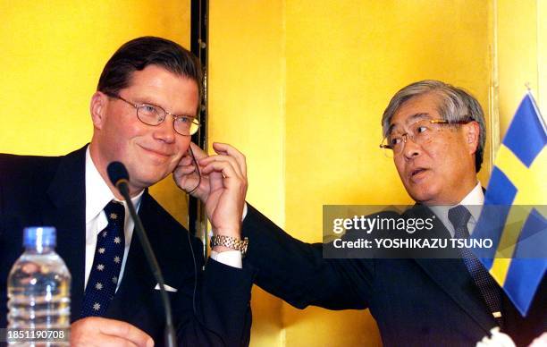 Swedish automaker Volvo President Leif Johansson is helped to plug an ear-phone by Japan's Mitsubishi Motors President Katsuhiko Kawasoe prior to...