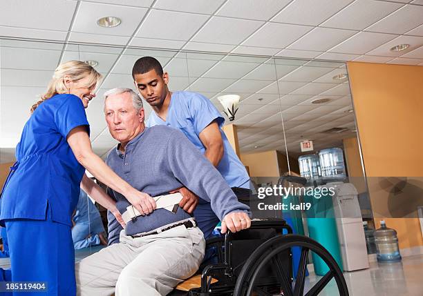 healthcare workers helping patient into wheelchair - lifting stockfoto's en -beelden