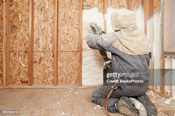 worker spraying expandable foam insulation between wall studs - house insulation not posing stockfoto's en -beelden
