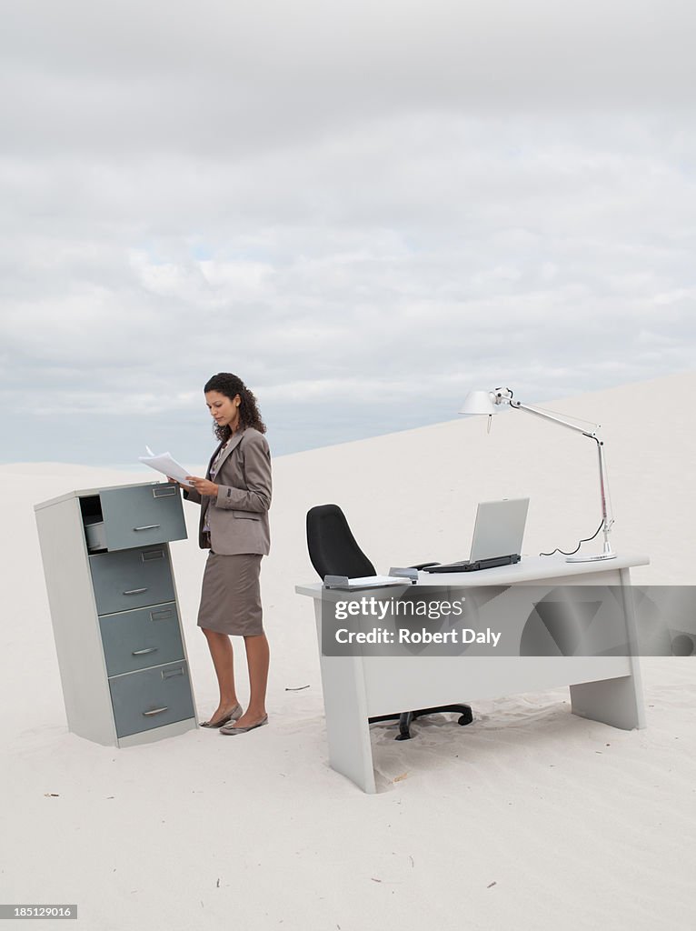 A businesswoman standing in the middle of a desert at her filing cabinet 