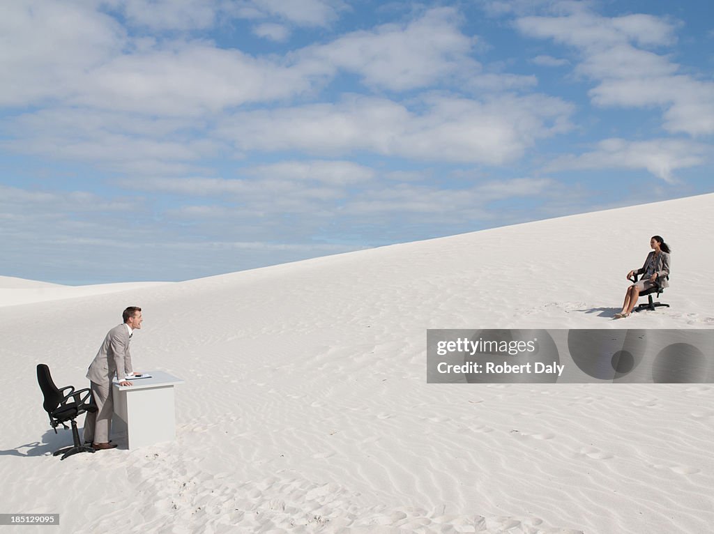 A businessman yelling to a businesswoman in the middle of a desert 
