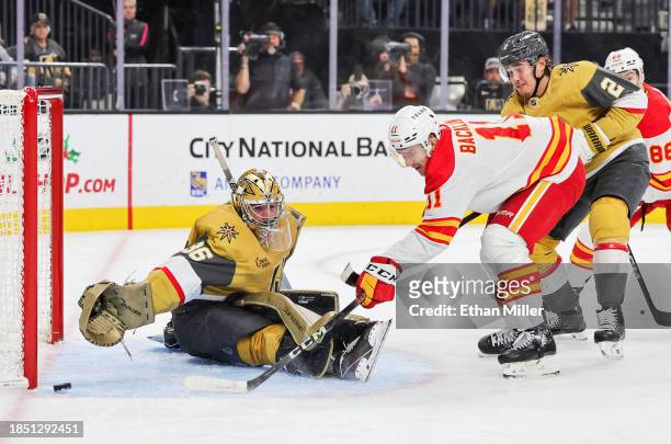 Mikael Backlund of the Calgary Flames puts a rebound wide of the net as Logan Thompson and Zach Whitecloud of the Vegas Golden Knights defend in the...