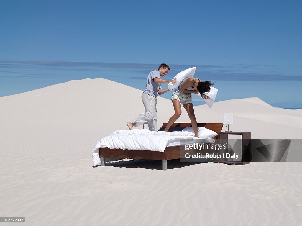 A couple on a bed having pillow fighting outdoors