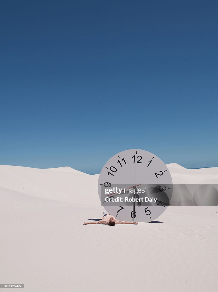 A man lying by a clock in the desert