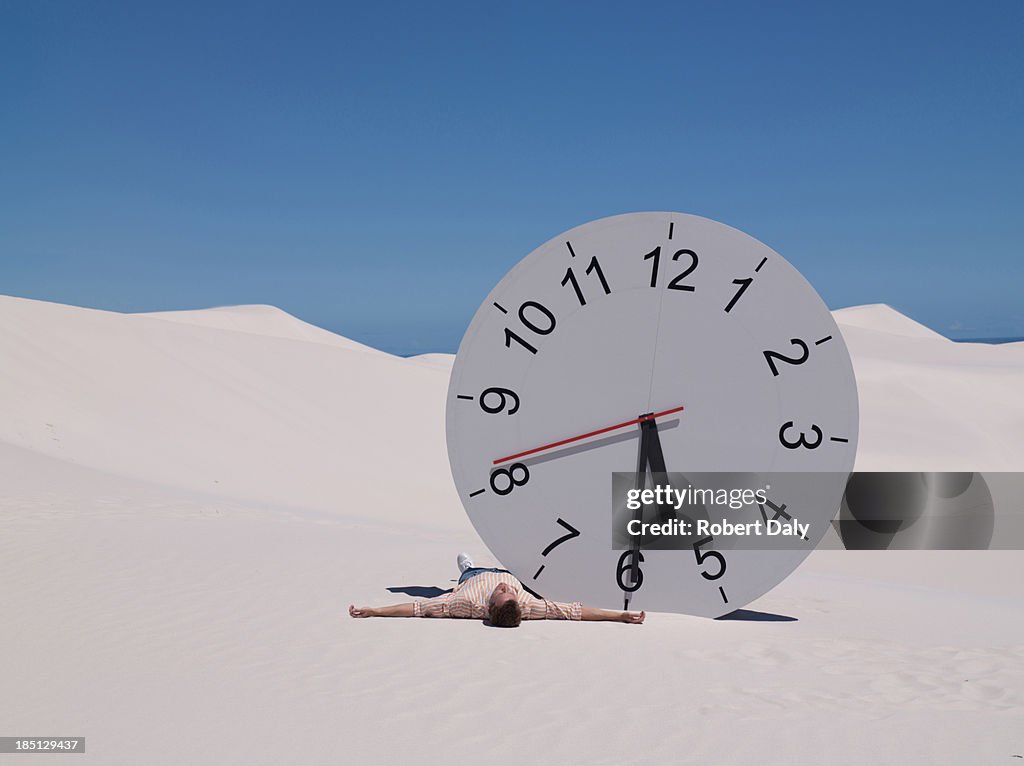 A man lying by a clock in the desert