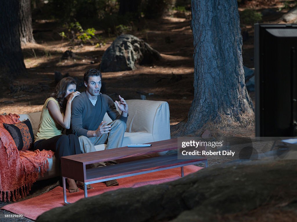 A couple sitting on coach watching television outdoors in the woods