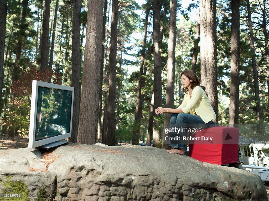 A woman watching television outdoors in the woods