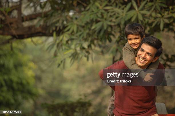 happy father piggybacking son in garden - indian people stock pictures, royalty-free photos & images