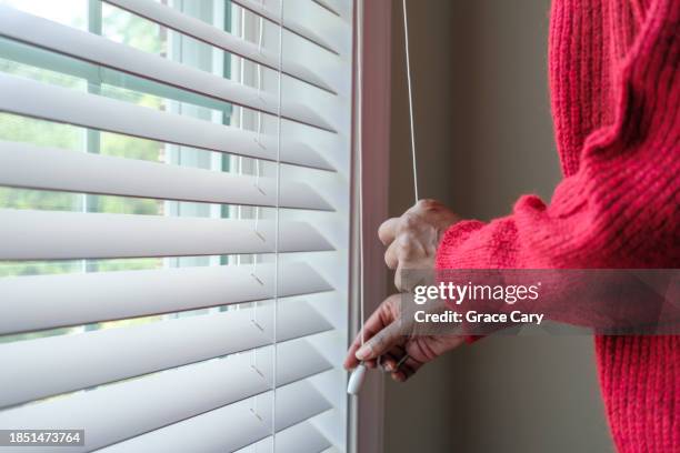 woman adjusts window blind - tapparella foto e immagini stock