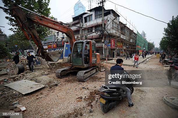 Man rides on a motorcycle past an excavator at a constriction site in Wuhan, China, on Thursday, Oct. 17, 2013. China is scheduled to release...