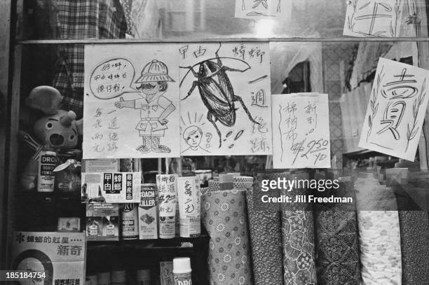 Shop window in Chinatown displays fabrics and pest control powder, New York City, 1977.