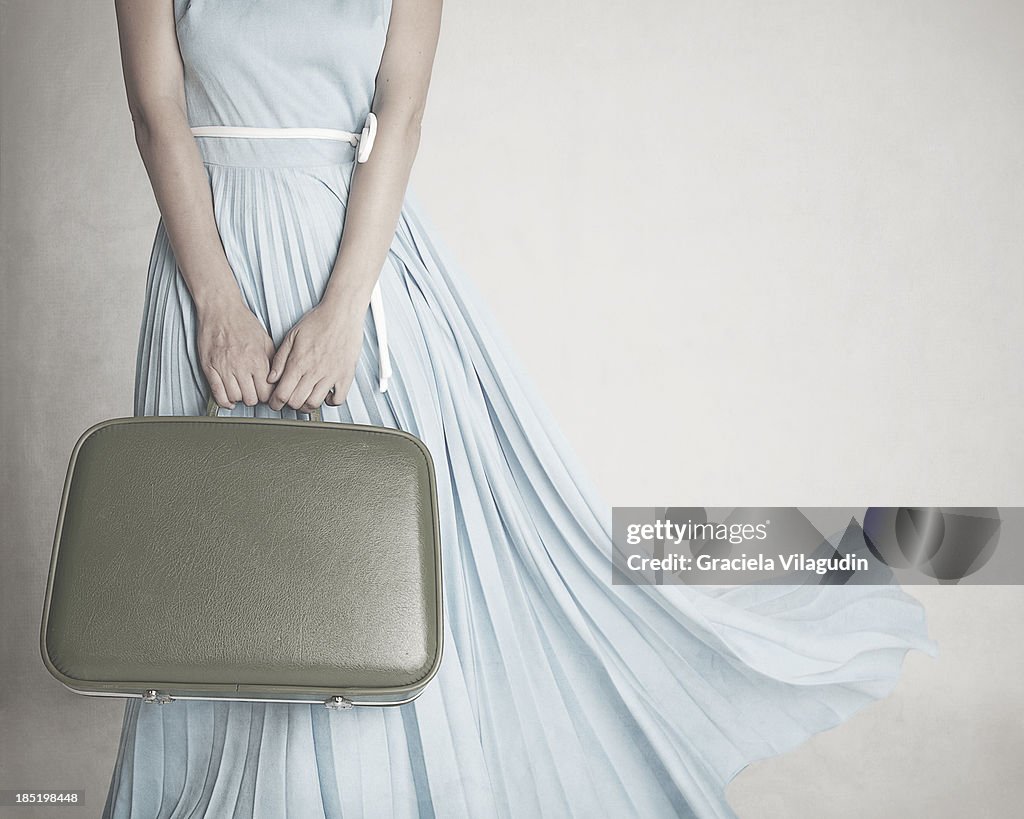 Girl with blue dress holding vintage suitcase