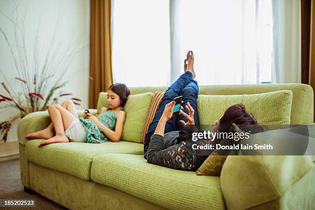 mother and daughter on phones - lying on back girl on the sofa stock pictures, royalty-free photos & images