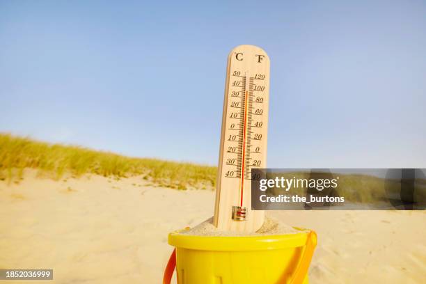 thermometer in a bucket at beach against sand dune and clear sky - chaleur photos et images de collection