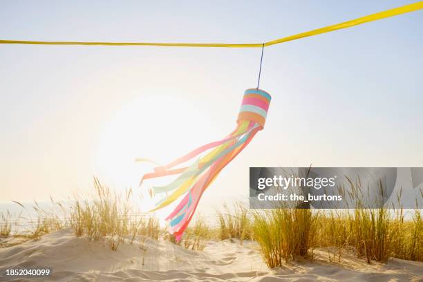 colorful self-made wind chime flying in the wind at sand dune against sea and sun - wind chime stock pictures, royalty-free photos & images