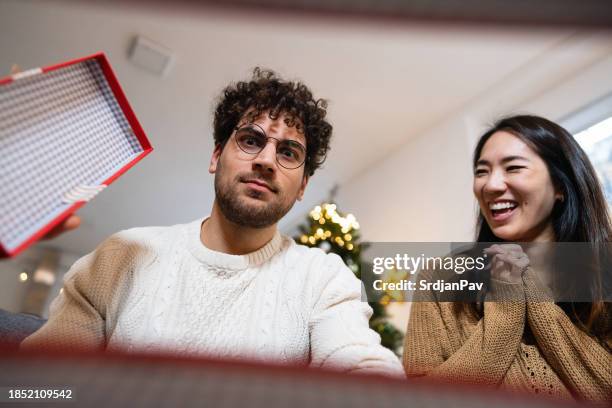 young couple opening christmas presents - disappointment gift stock pictures, royalty-free photos & images