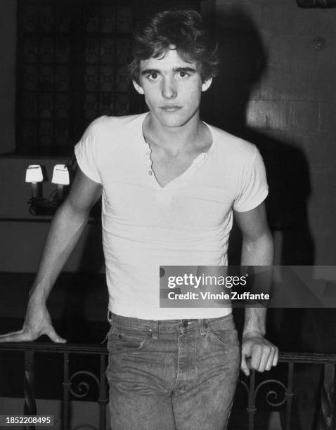 American actor Matt Dillon, wearing a white cap-sleeved t-shirt and jeans, leaning on a metalwork balustrade, United States, circa 1983.