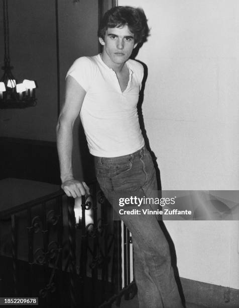 American actor Matt Dillon, wearing a white cap-sleeved t-shirt and jeans, leaning on a metalwork balustrade, United States, circa 1980.