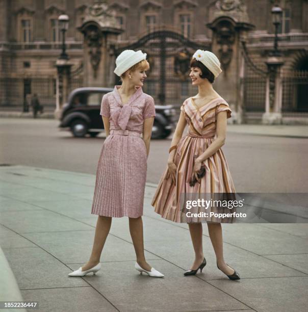 Two female fashion models posed wearing, on left, a pale pink marl belted dress with pleated skirt and bow collar and, on right, a pink, yellow and...