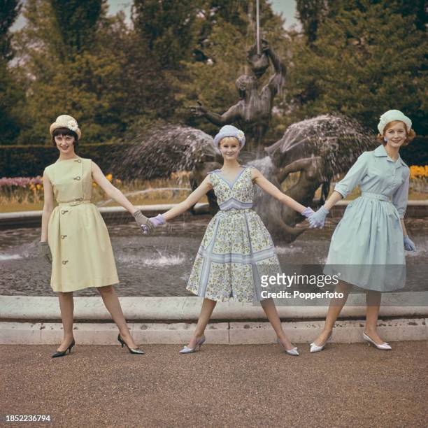Three female fashion models posed wearing cool pastel coloured dresses, from left, a sleeveless knee length belted light yellow dress with buttons, a...