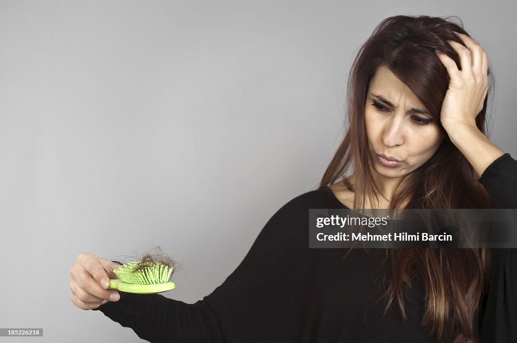 A long hair woman holding a green hairbrush full of hairs