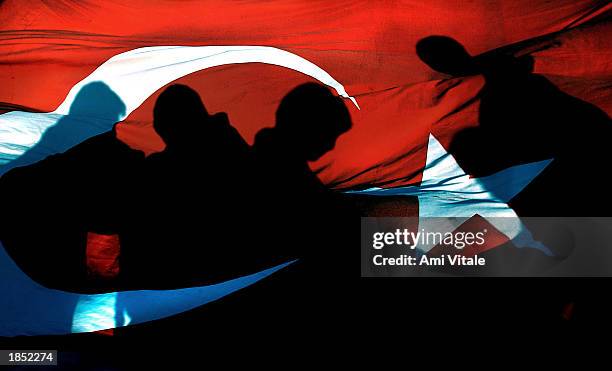 Turkish anti-war protesters' shadows are cast on a Turkish flag at a rally in the port city of Iskenderun, Turkey March 15, 2003. The Turkish Prime...