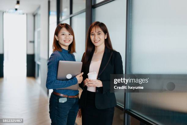 dos mujeres de negocios asiáticas en una oficina moderna sonriendo y mirando a la cámara - estereotipo fotografías e imágenes de stock