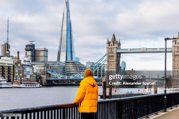 man wearing warm yellow winter jacket looking at london skyline, rear view, uk - london city hall stock pictures, royalty-free photos & images