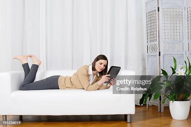 brunette mujer con tablet pc en sofá blanco - mujeres de mediana edad fotografías e imágenes de stock