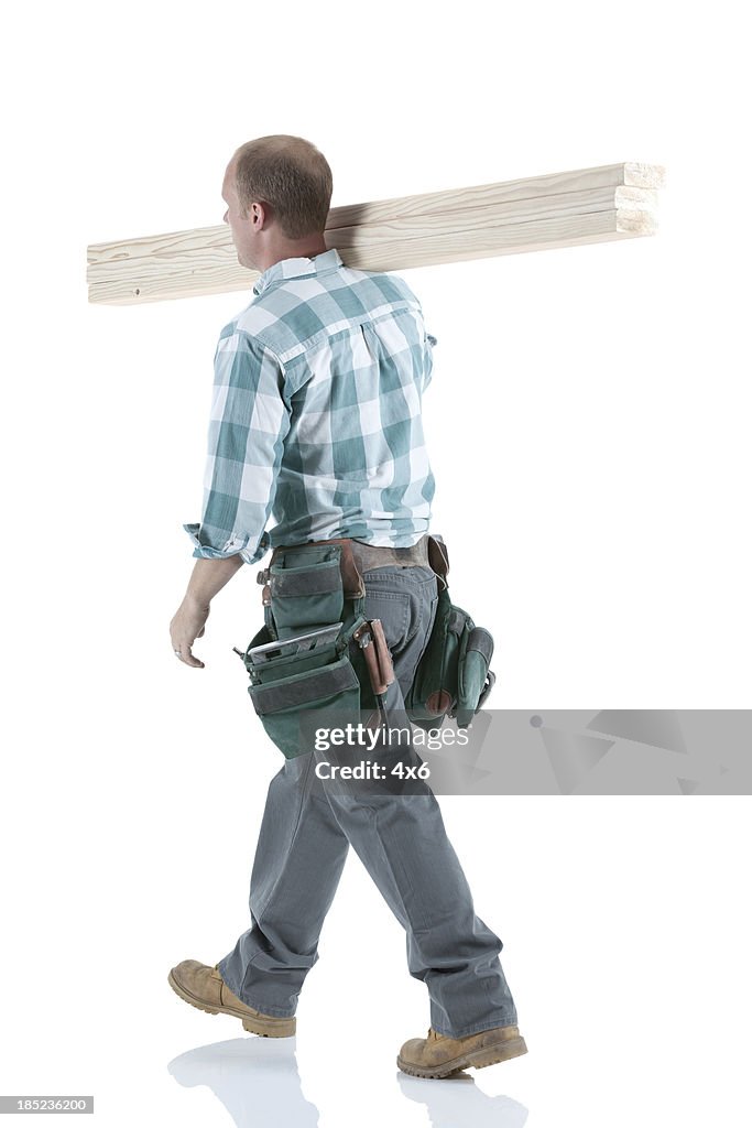 Carpenter carrying wooden planks on his shoulders