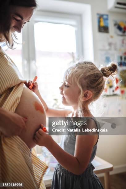 family expansion: joyful girl child drawing on mom's pregnant belly, awaiting new addition at home. sunny photo. - human body part stock pictures, royalty-free photos & images