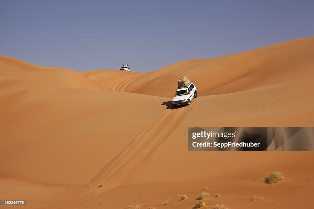 Car driving in the desert between sand dunes