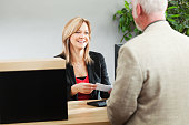 Bank Teller Serving Customer Over Retail Banking Service Counter