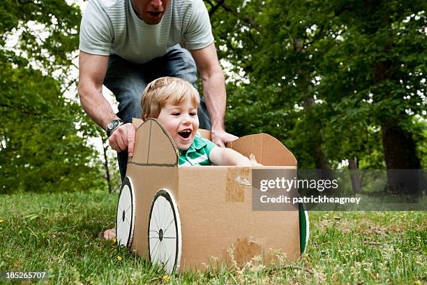 padre spingendo il suo figlio in una scatola di cartone in erba - toddler in car foto e immagini stock