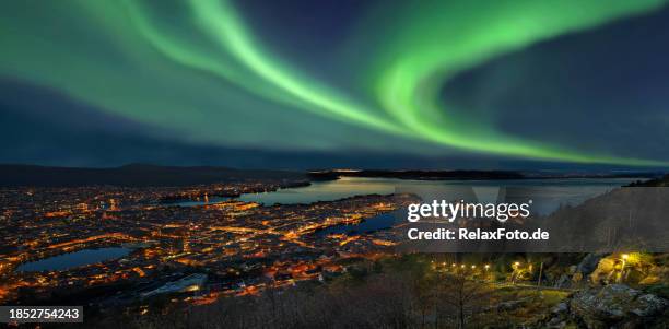 vista dall'alto sul porto della città illuminata di bergen con la maestosa aurora boreale verde - bergen foto e immagini stock