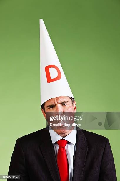 businessman in dunce cap sticks out his tongue - dunce cap stock pictures, royalty-free photos & images