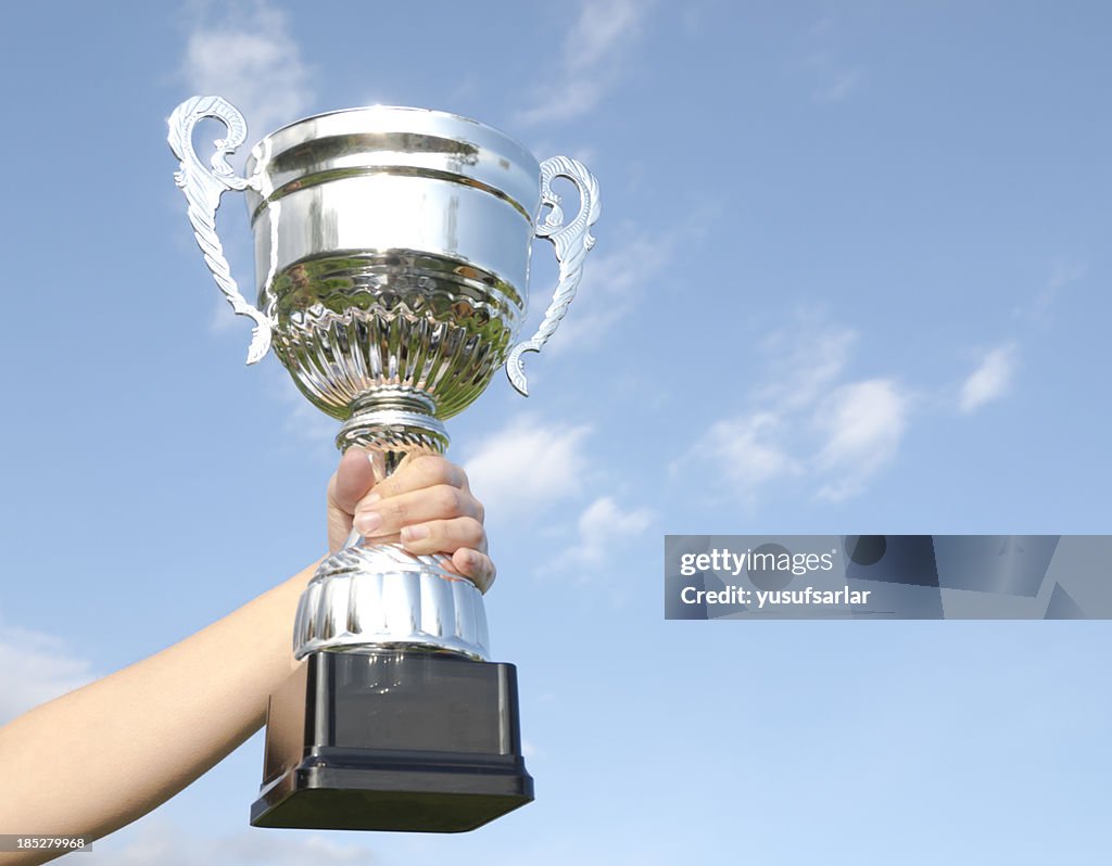 Hand holding a trophy with a blue sky on the background